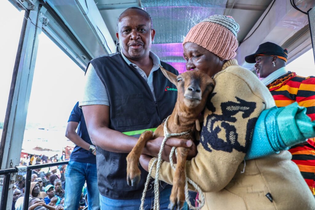 Samuel Kirubi, Rift Valley Regional Business Lead at Safaricom (Left) awards Sally Tembur (Right) a goat courtesy of the ongoing Safaricom Sambaza Furaha campaign at Kapsoit Market in Kericho County. The campaign seeks to delight customers across the country with gifts during this festive season.