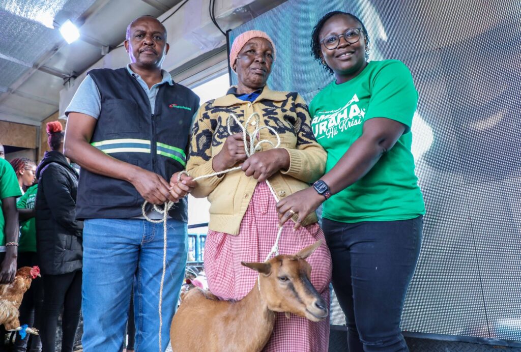 Samuel Kirubi, Rift Valley Regional Business Lead at Safaricom (Left) and Stella Arithi, Chapter Lead for Integrated Media at Safaricom (Right) awards Sally Tembur a goat courtesy of the ongoing Safaricom Sambaza Furaha campaign at Kapsoit Market in Kericho County. The campaign seeks to delight customers across the country with gifts during this festive season.